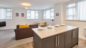 Un appartement moderne doté d’un îlot central dans la cuisine, d’un canapé marron et d’un coin repas avec une table dressée pour quatre personnes.