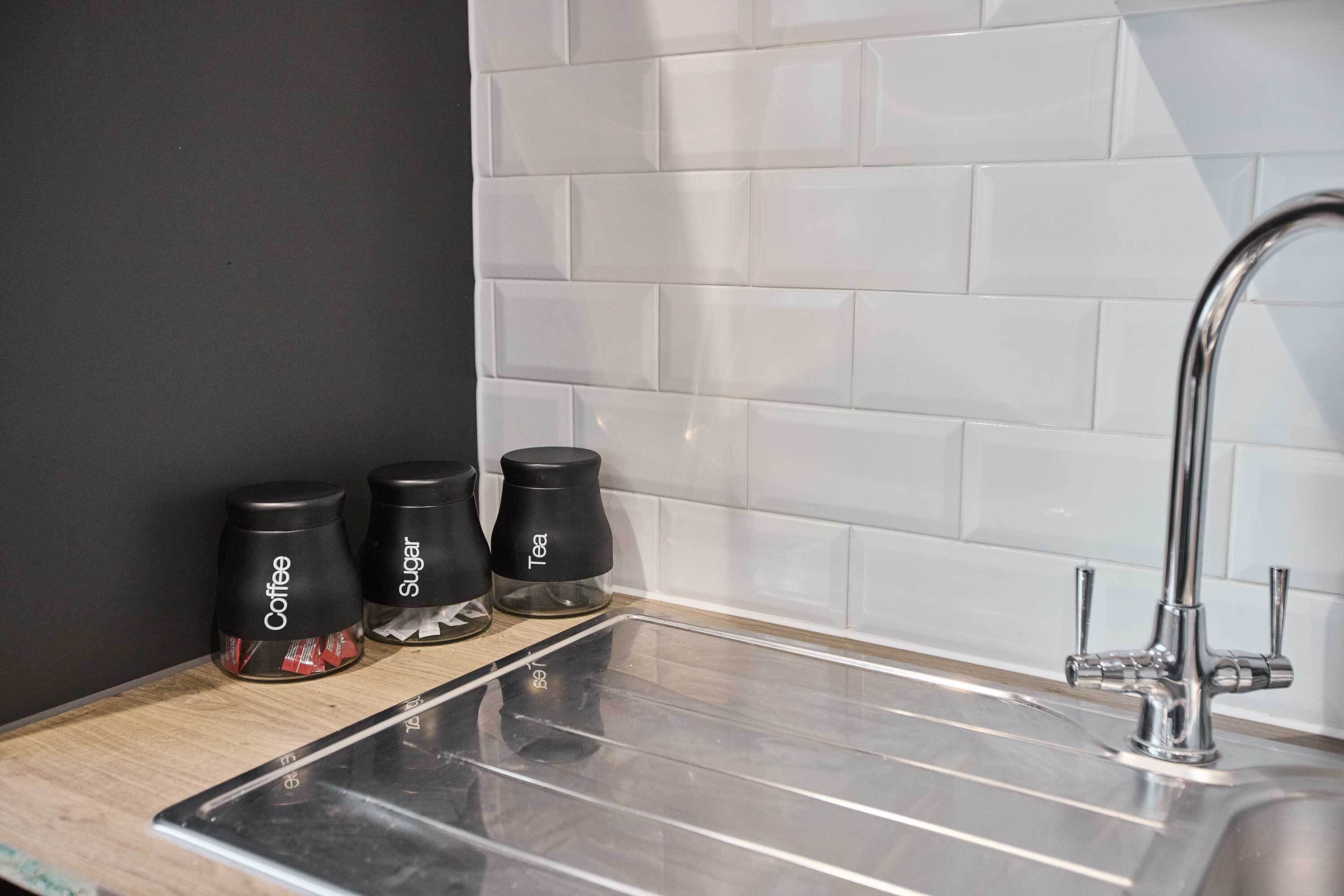 A kitchen with a stainless steel sink, a wooden countertop, and three black containers labeled coffee, sugar, and tea.
