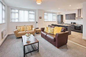 A modern living room with two sofas, a coffee table, and a kitchen area with cabinets and a stove. - Host & Stay | Promenade Suite (Blackpool)