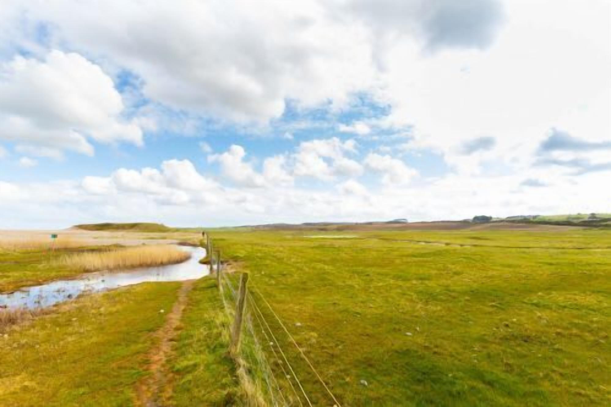 Un vaste champ ouvert, avec un petit plan d’eau et une clôture qui le traverse.