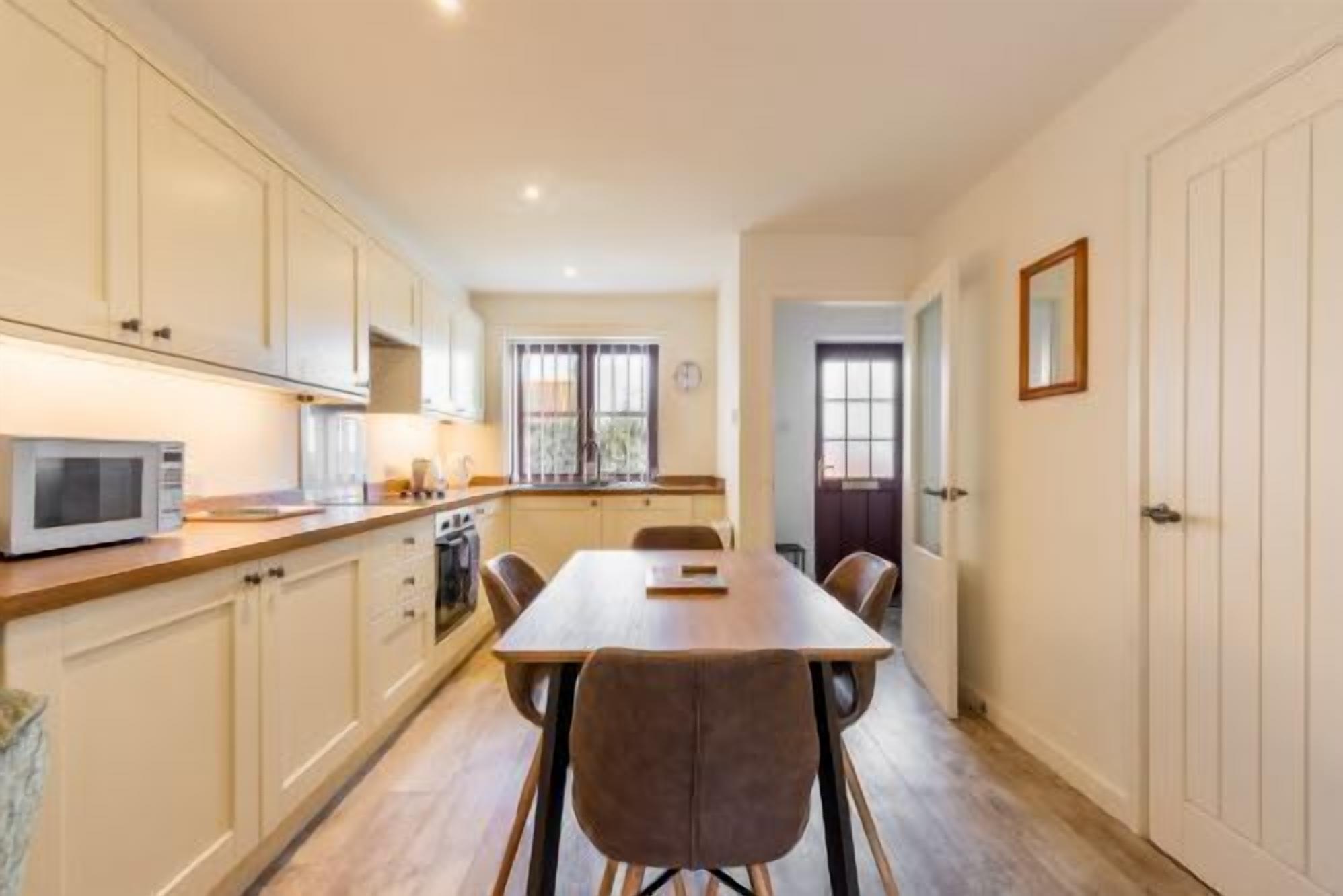 Una cucina moderna con mobili bianchi, un forno a microonde e una zona pranzo con tavolo e sedie in legno.