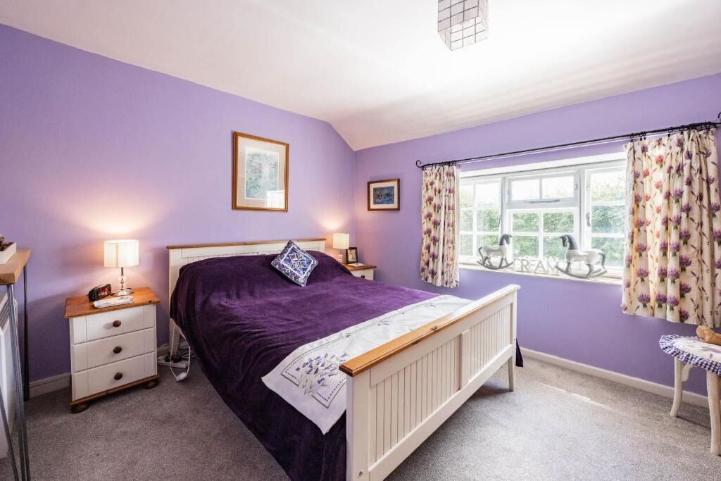 A bedroom with a bed, a nightstand, a dresser, a window with curtains, and a chair.