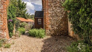 Ein schmaler Gang mit Kiesweg, Steinwänden und einem Holzhaus mit Ziegeldach.