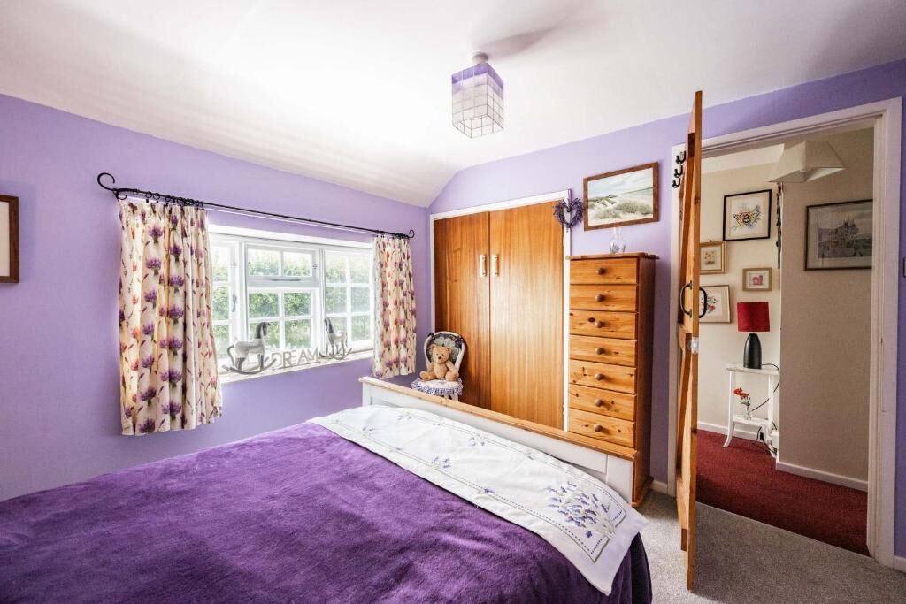A bedroom with a bed, a wardrobe, a window with curtains, and a door leading to another room.