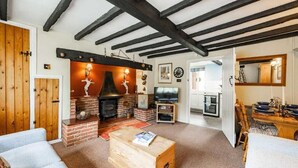 Ein gemütliches Wohnzimmer mit freiliegenden Holzbalken, einem Kamin, einem Fernseher und einem Essbereich mit Tisch und Stühlen.