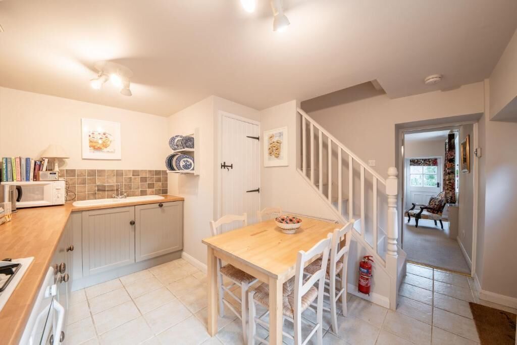 A kitchen with white cabinets, a wooden table, and a staircase leading to a dining area.