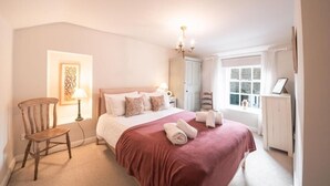 Een keurig opgemaakt slaapkamer met een groot bed, een stoel, een nachtkastje en een raam met gordijnen.