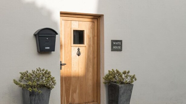 Een houten deur met een brievenbus en een bordje met daarop 'WHITE HOUSE' op een witte muur.