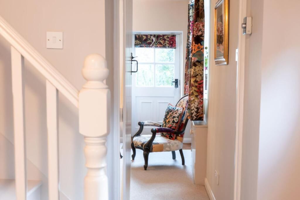 A hallway with a white staircase, a door with a floral curtain, and a chair with a patterned cushion.