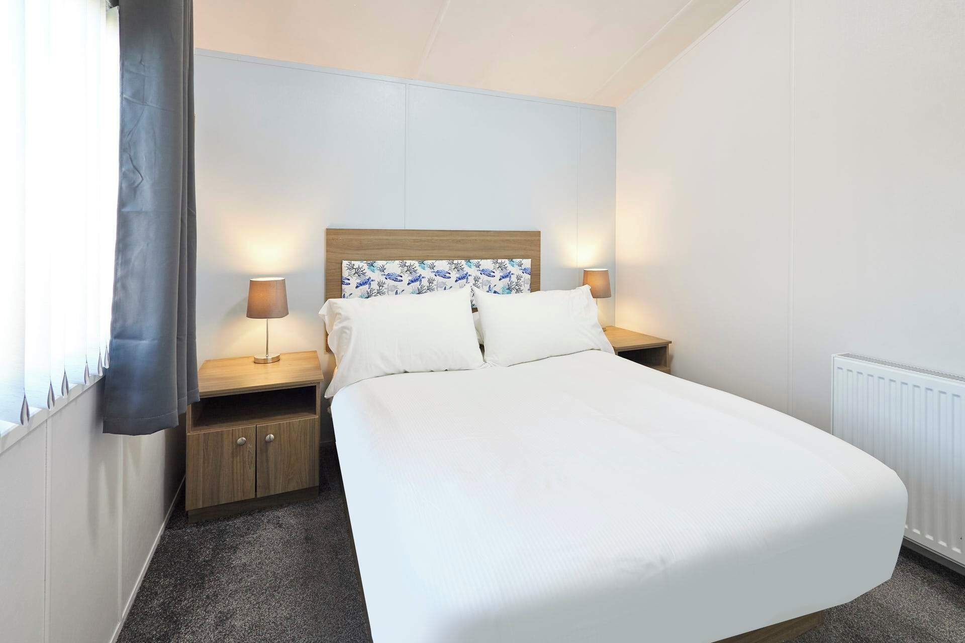 Een hotelkamer met een bed, twee nachtkastjes met lampen, een hoofdbord met bloemendesign en een radiator.