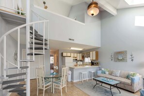 A modern interior with a spiral staircase, a kitchen with white cabinets, a dining area with a glass table, and a sofa with a patterned throw. - Large 2BR Private Condo, Surfside, Beautiful Decor (Surfside Beach)