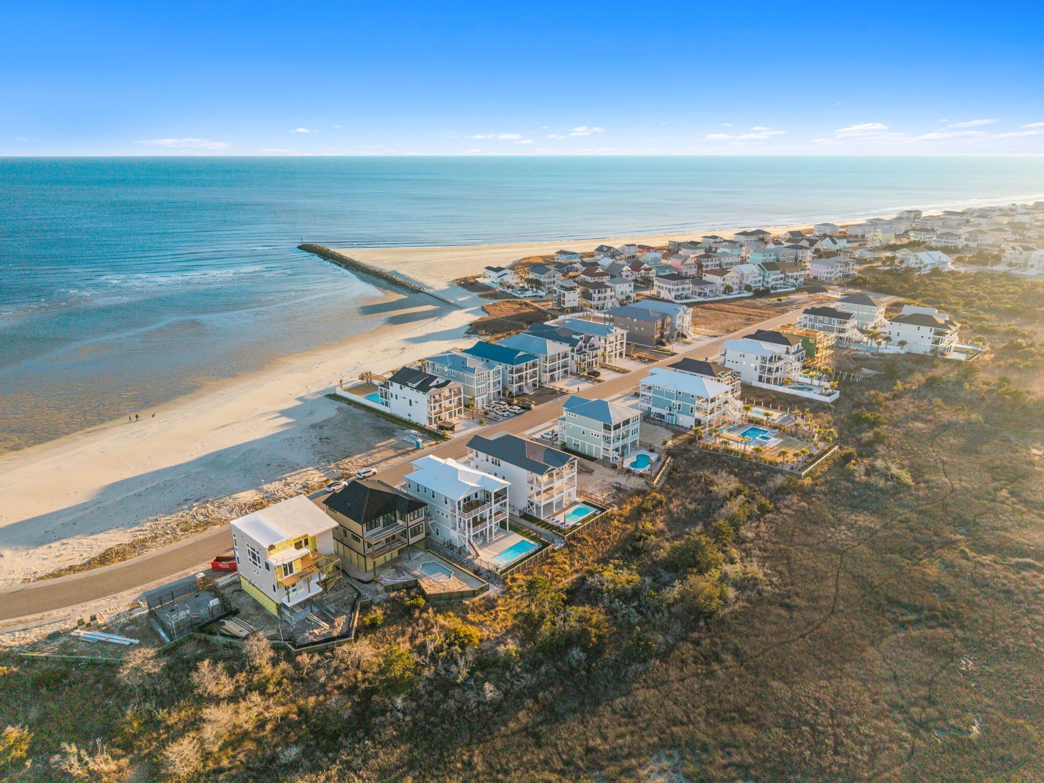 An aerial view of a coastal residential area with houses, a beach, and a pier.