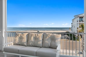 Ein Balkon mit einer beigen Couch und Blick auf Strand und Meer.