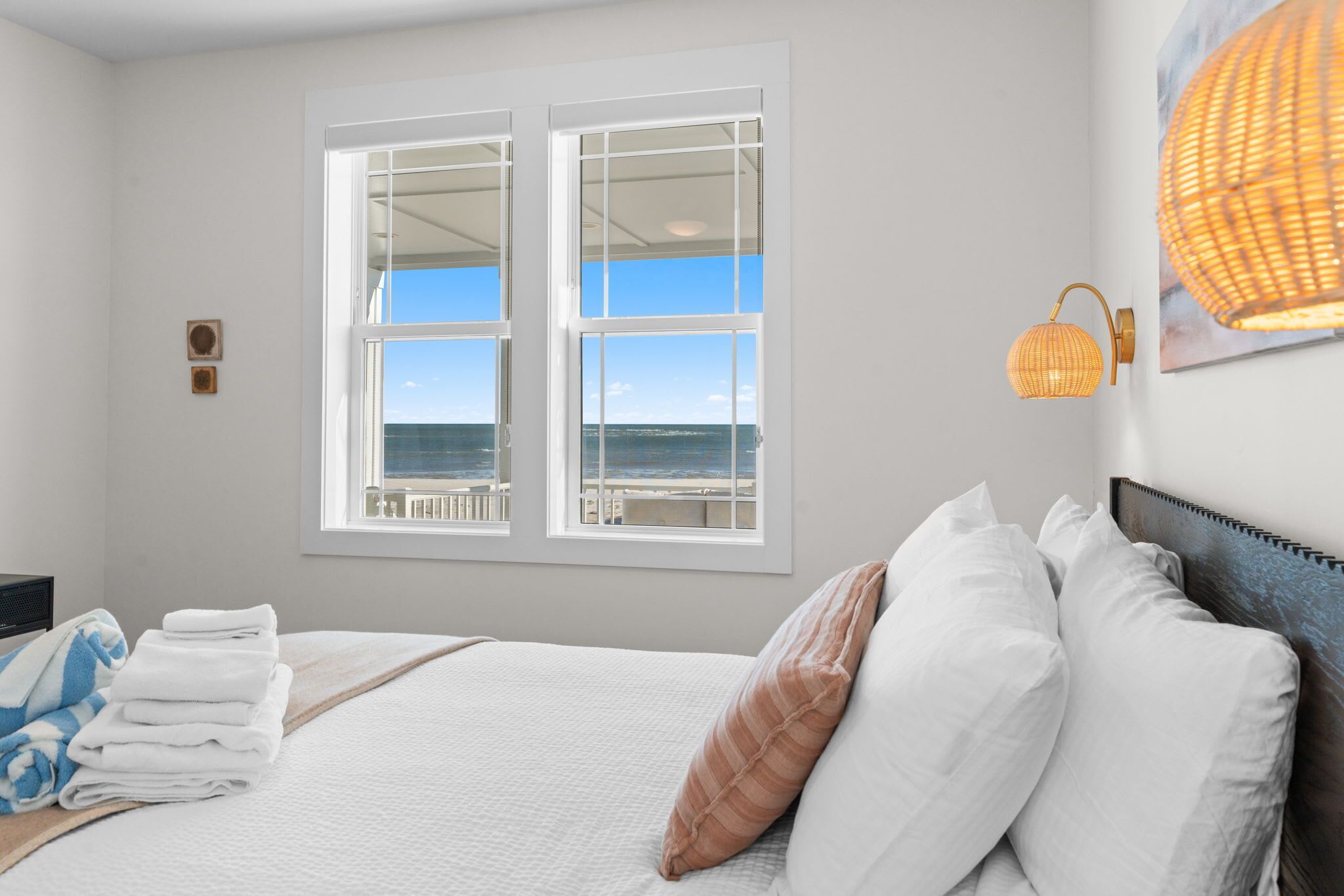 Une chambre d’hôtel avec un lit, une vue sur la mer grâce à de grandes fenêtres, une lampe fixée au mur et un tableau encadré.