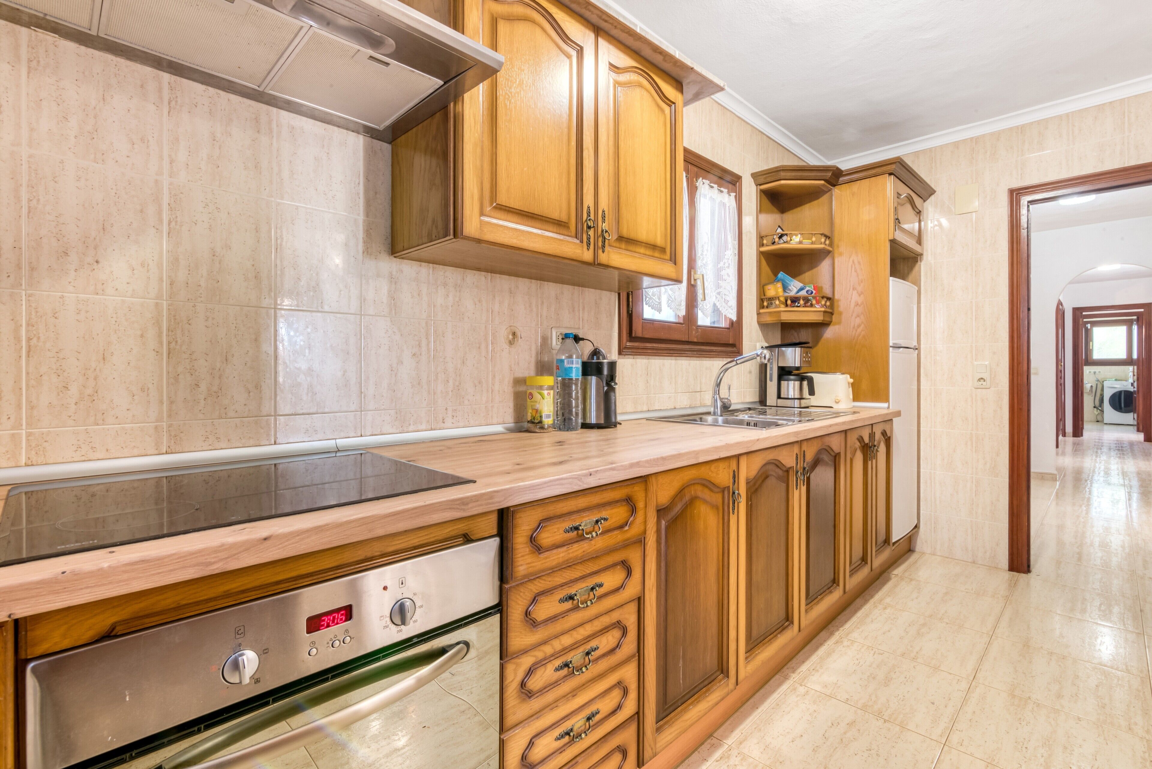 Cocina con armarios de madera, campana extractora de acero inoxidable, horno empotrado y encimera con lavaplatos.