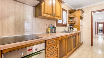 Cocina con armarios de madera, campana extractora de acero inoxidable, horno empotrado y encimera con lavaplatos.