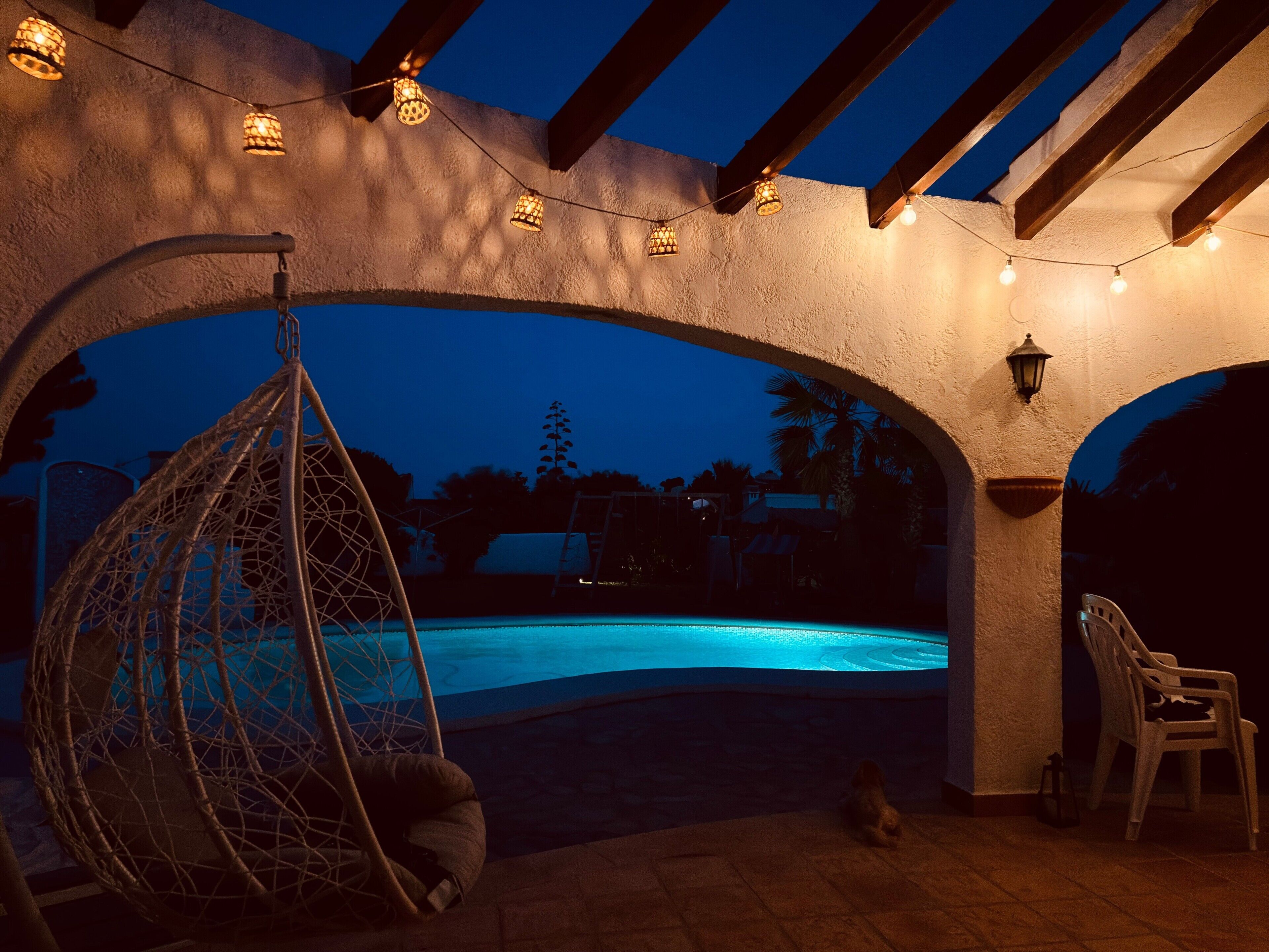 Un área de piscina con una hamaca colgante, una silla y luces de cuerda.