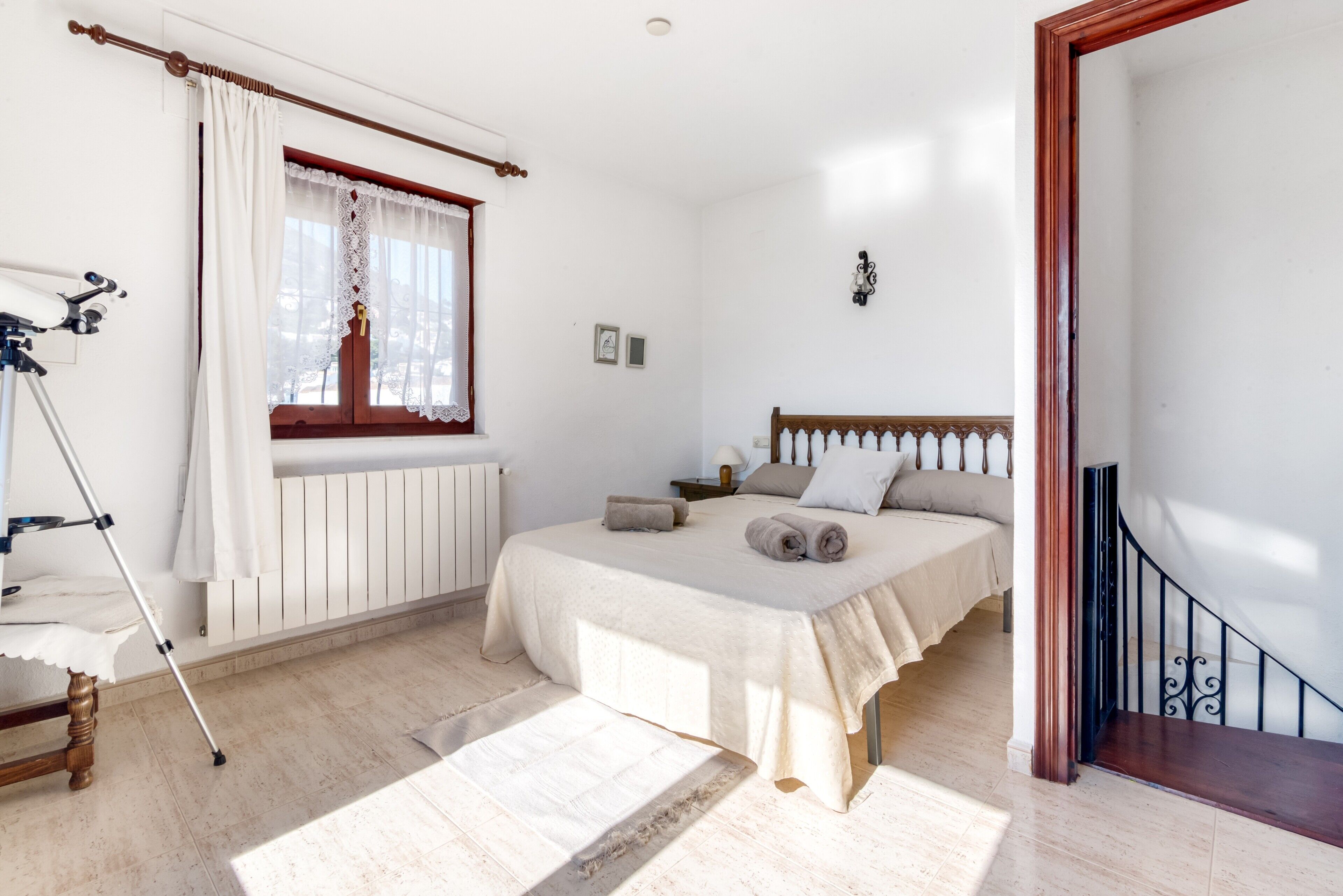 Een slaapkamer met een bed, een raam met gordijnen, een nachtkastje, een lamp en een telescoop.