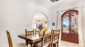 Un comedor con una mesa y sillas de madera, un jarrón con flores y vistas a un balcón a través de un arco.
