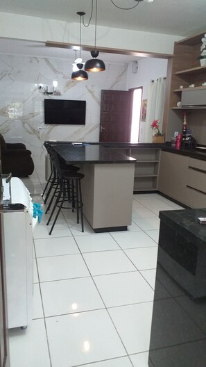 A modern kitchen with a central island, bar stools, a flat-screen TV, and a wooden door.