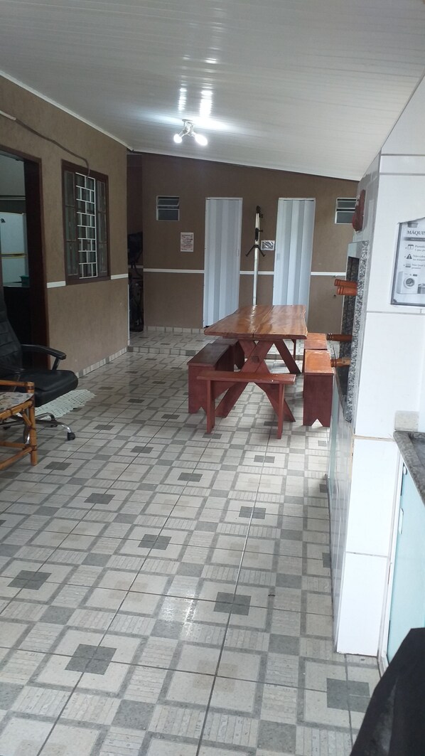 A room with a large wooden table and benches, a ceiling fan, and a tiled floor.
