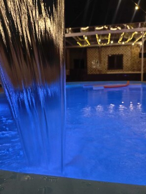 A swimming pool with a waterfall feature and a building in the background.