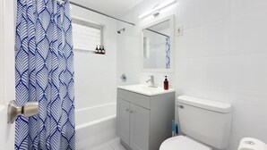 A bathroom with a bathtub, toilet, sink, and a shower curtain. - 1BR Miami Beach Apt w/ King + 2 Queens & Smart TV (Miami Beach)