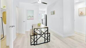 A modern interior with a dining table, chairs, a ceiling fan, and a kitchen area in the background. - 1BR Miami Beach Apt w/ King + 2 Queens & Smart TV (Miami Beach)