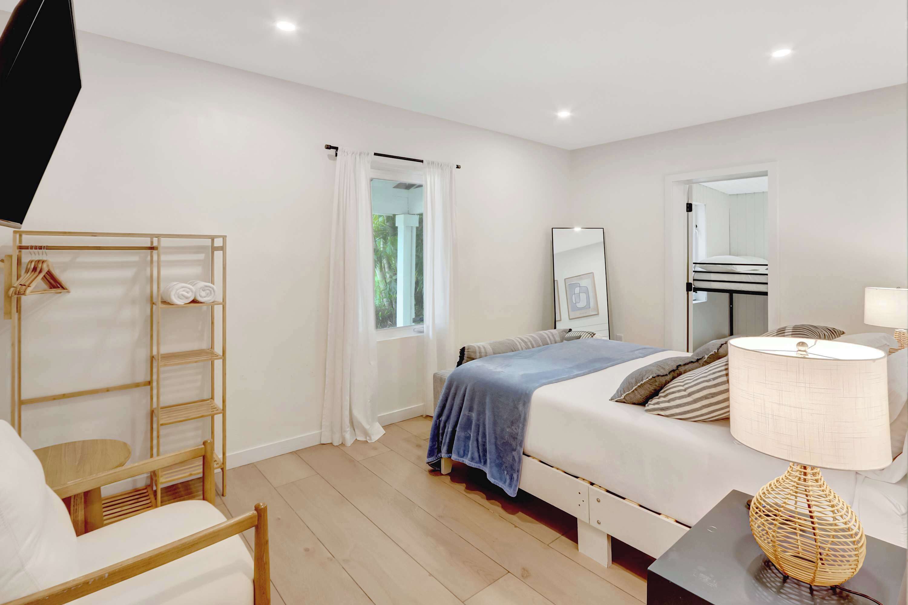 Une chambre à coucher avec un lit, une table de chevet avec une lampe, une armoire, une fenêtre avec des rideaux et un miroir au mur.