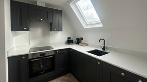 Een moderne keuken met donkere kasten, een wit aanrecht, een ingebouwde oven, een zwarte spoelbak en een dakraam.