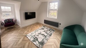 Een moderne loft slaapkamer met een visgraatparketvloer, een groot raam, een groene bank, een gekleurd vloerkleed en een wandgemonteerde televisie.