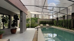 An indoor swimming pool with a glass barrier, potted plants, and lounge chairs. - Vitrali Moema (São Paulo)