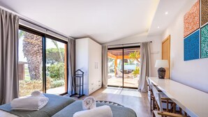 Ein Hotelzimmer mit zwei Betten, einem Schreibtisch und Blick auf einen Außenbereich mit Pool und Liegestühlen.