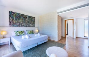 Une chambre d’hôtel moderne avec un grand lit, deux tables de chevet, une œuvre d’art murale et une vue sur le couloir.