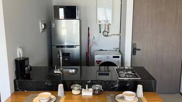 Cozinha compacta equipada com frigorífico, micro-ondas e máquina de café.