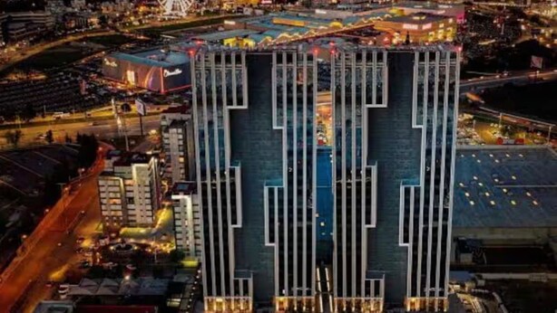 A modern hotel with a distinctive vertical design, located in a bustling urban area with a Ferris wheel in the background. - Loft 1 Boudica, Puebla (San Bernardino Tlaxcalancingo)