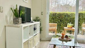 A modern living room with a glass table, a patterned rug, a flat-screen TV, and a large window with a view of a garden. - Apartment in Pucon (Pucon)