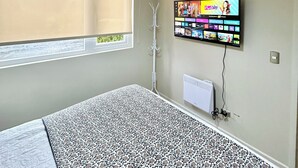 A room with a bed, a TV mounted on the wall, a window with blinds, and a radiator. - Apartment in Pucon (Pucon)