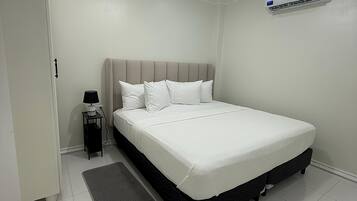 Une chambre bien rangée, avec un lit, une table de chevet, une lampe et un appareil de climatisation.