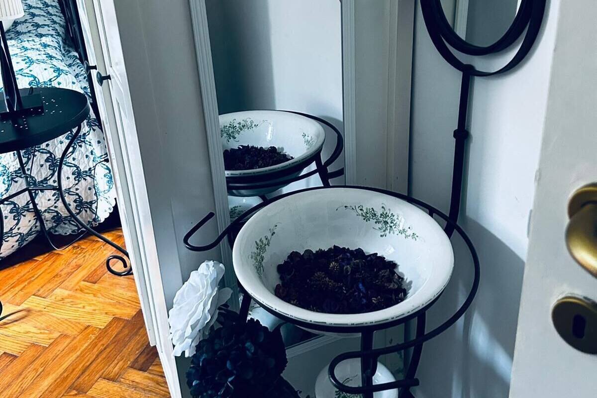 Un baño con un lavamanos blanco, un espejo y un inodoro. Hay una planta en maceta y una mesita con una lámpara.