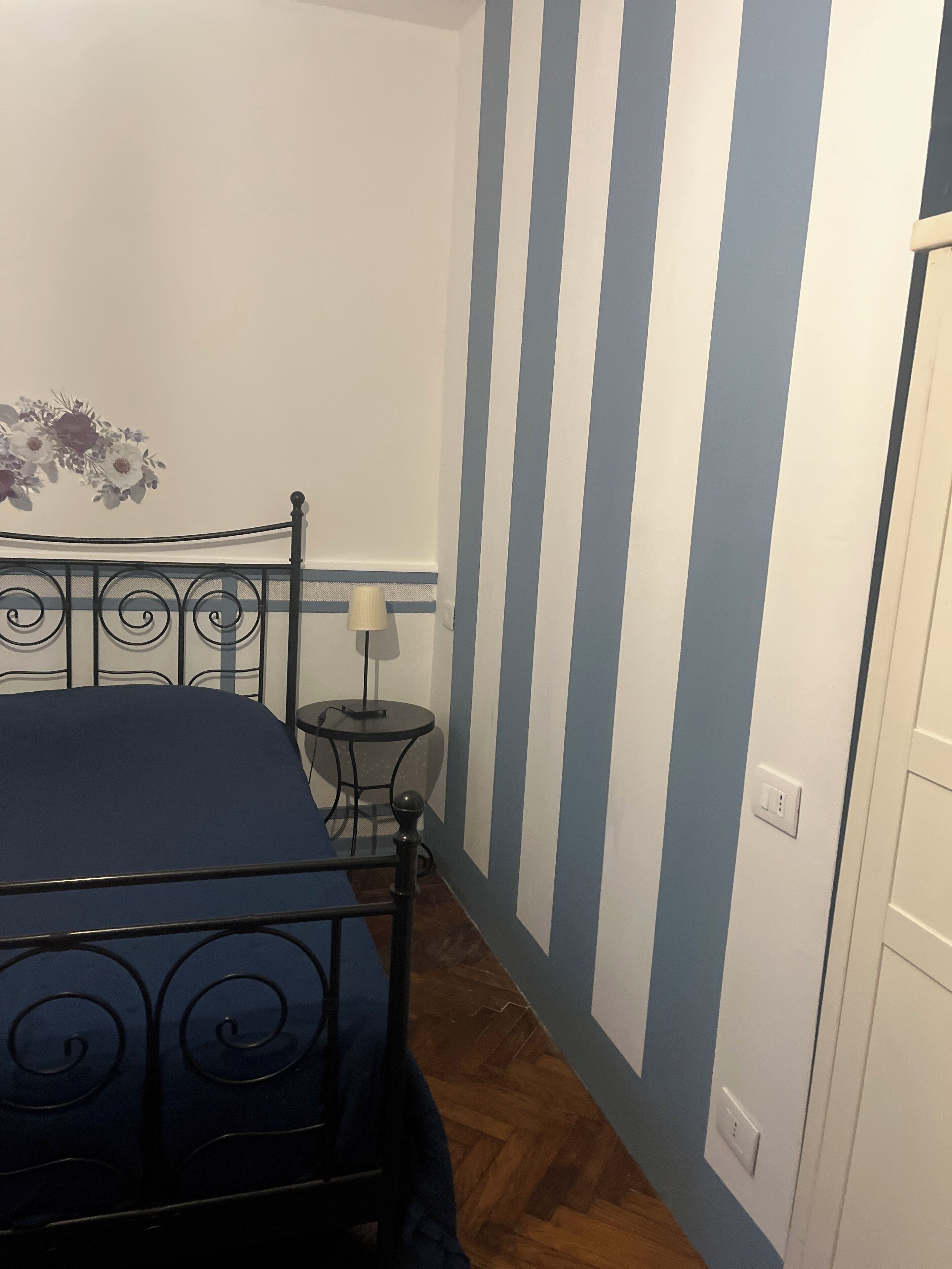 Een slaapkamer met een bed, een klein tafeltje met een lamp en een wand met verticale strepen.