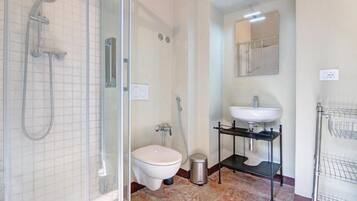 Een badkamer met een douchecabine van glas, een toilet, een wastafel en een spiegel.