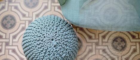 A round, knitted ottoman in a light blue color on a patterned floor.