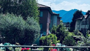 Una terraza con mesas y sillas de madera, rodeada de abundante vegetación y montañas al fondo.
