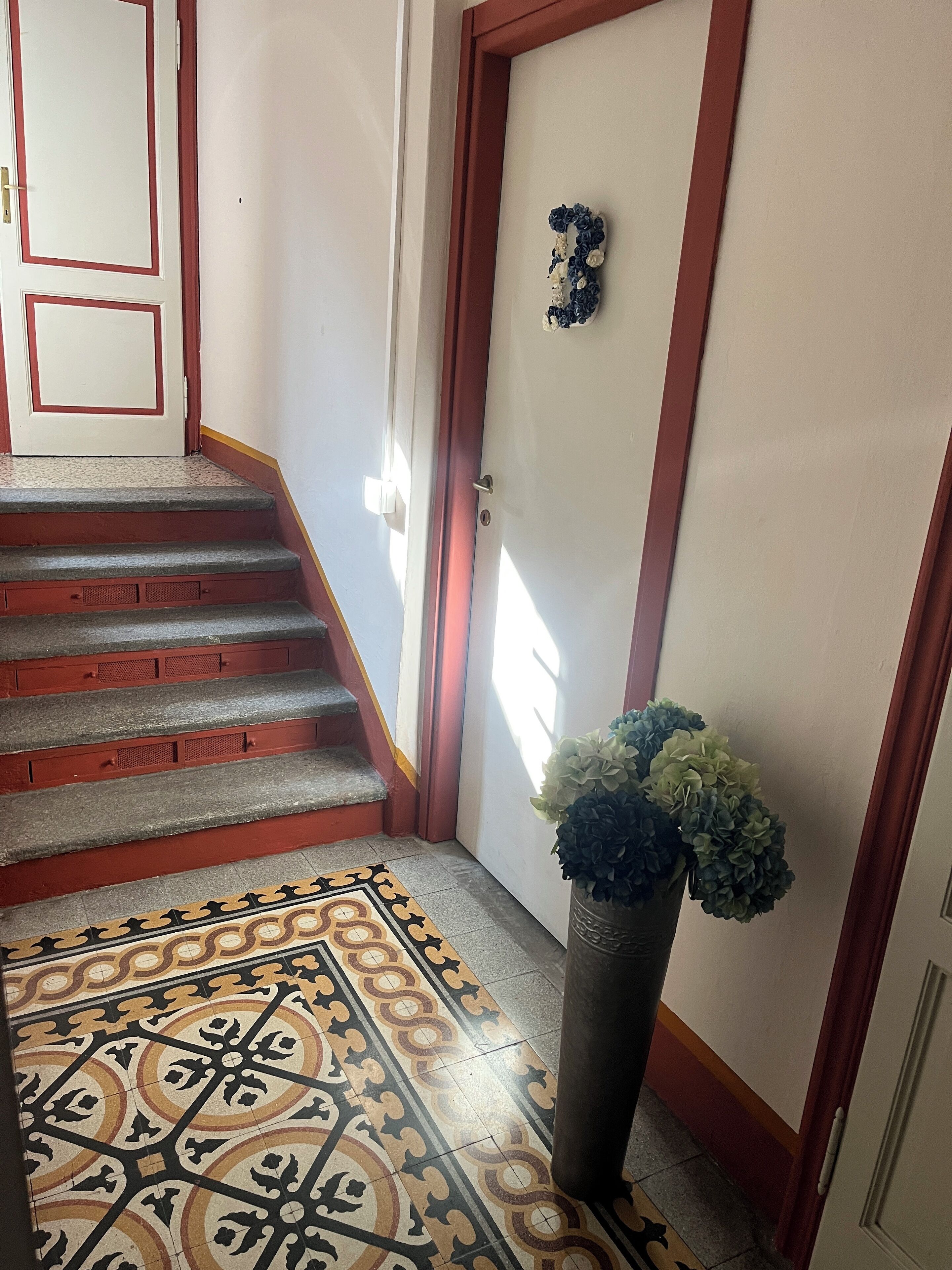 Una escalera con escalones rojos que conduce a una puerta, un suelo con diseño y una planta en maceta.
