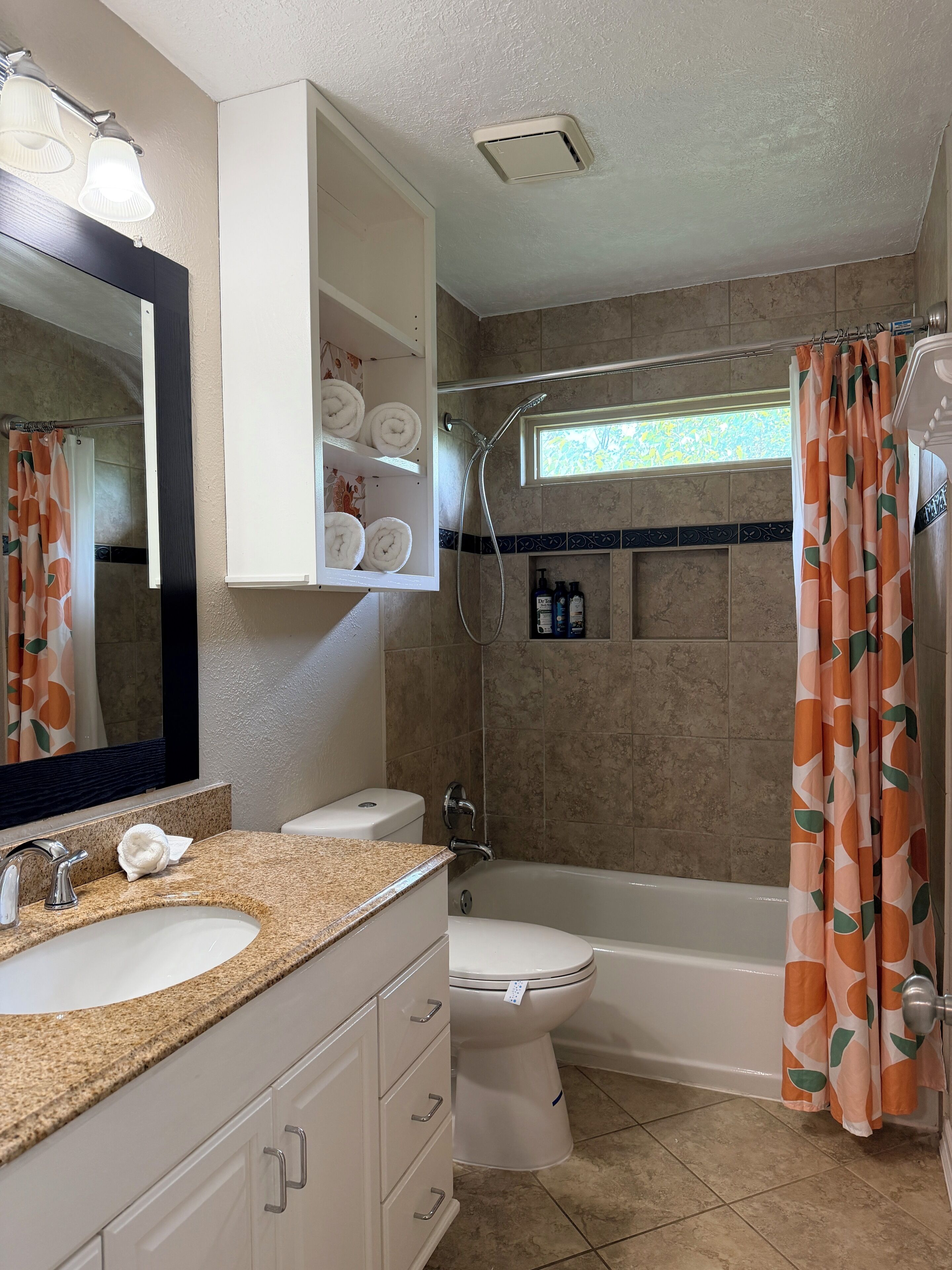 A bathroom with a sink, toilet, shower, and a mirror with a towel rack above it.