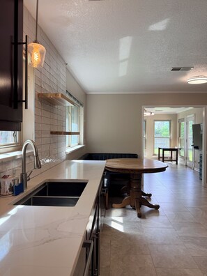 A kitchen with a marble countertop, a wooden dining table, and a hanging light fixture. - Stylish Modern Home / Big Group Getaway Sleeps 16 (Flower Mound)