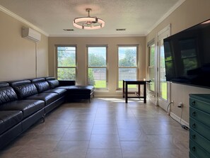 A living room with a sectional sofa, a dining table, a TV, and large windows. - Stylish Modern Home / Big Group Getaway Sleeps 16 (Flower Mound)