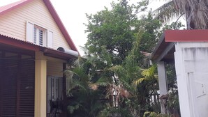 A house with a red roof, a covered porch, and a large tree in the background. - La Kaz Thomas (Saint-Leu)