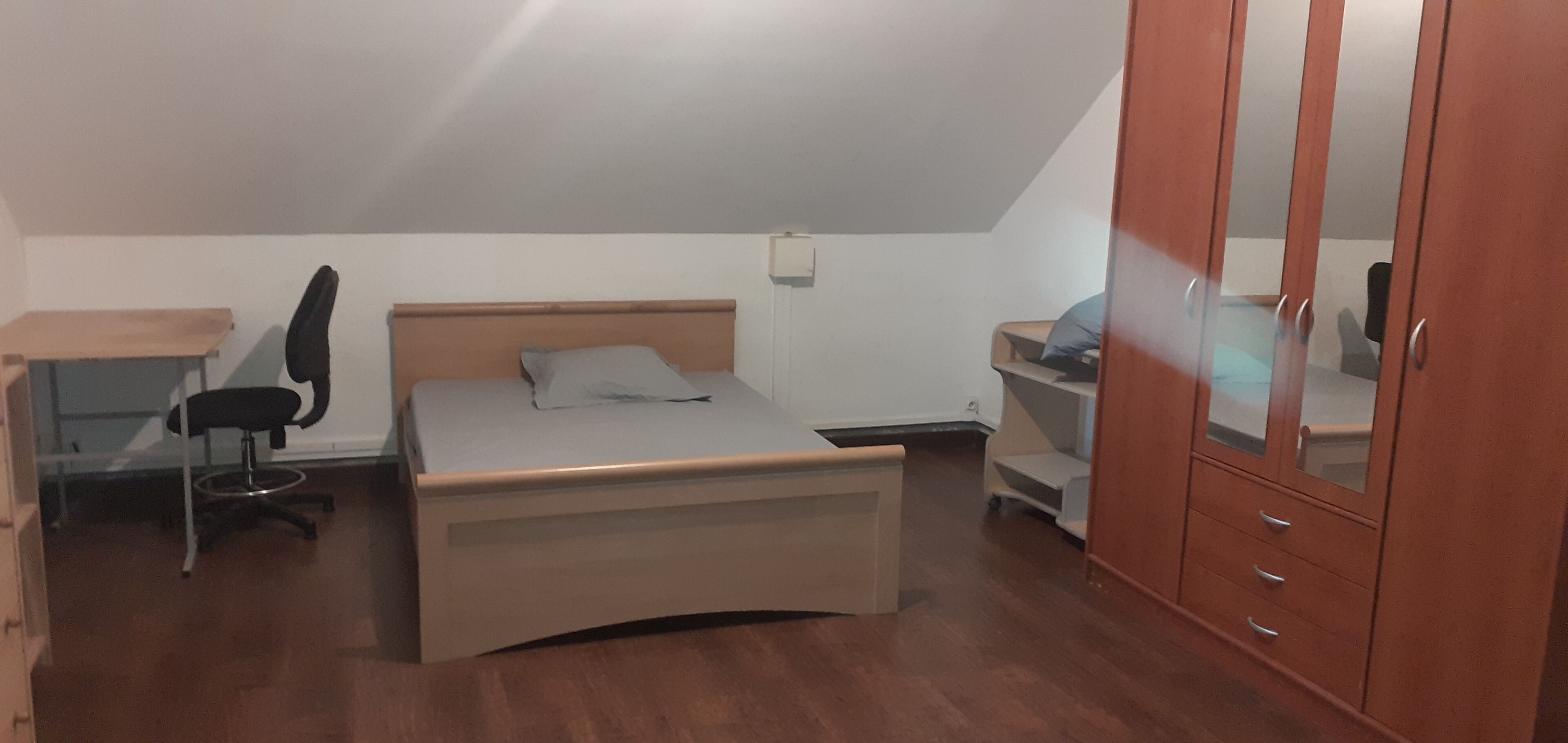 A bedroom with a bed, a desk, a chair, a wardrobe, and a small table.